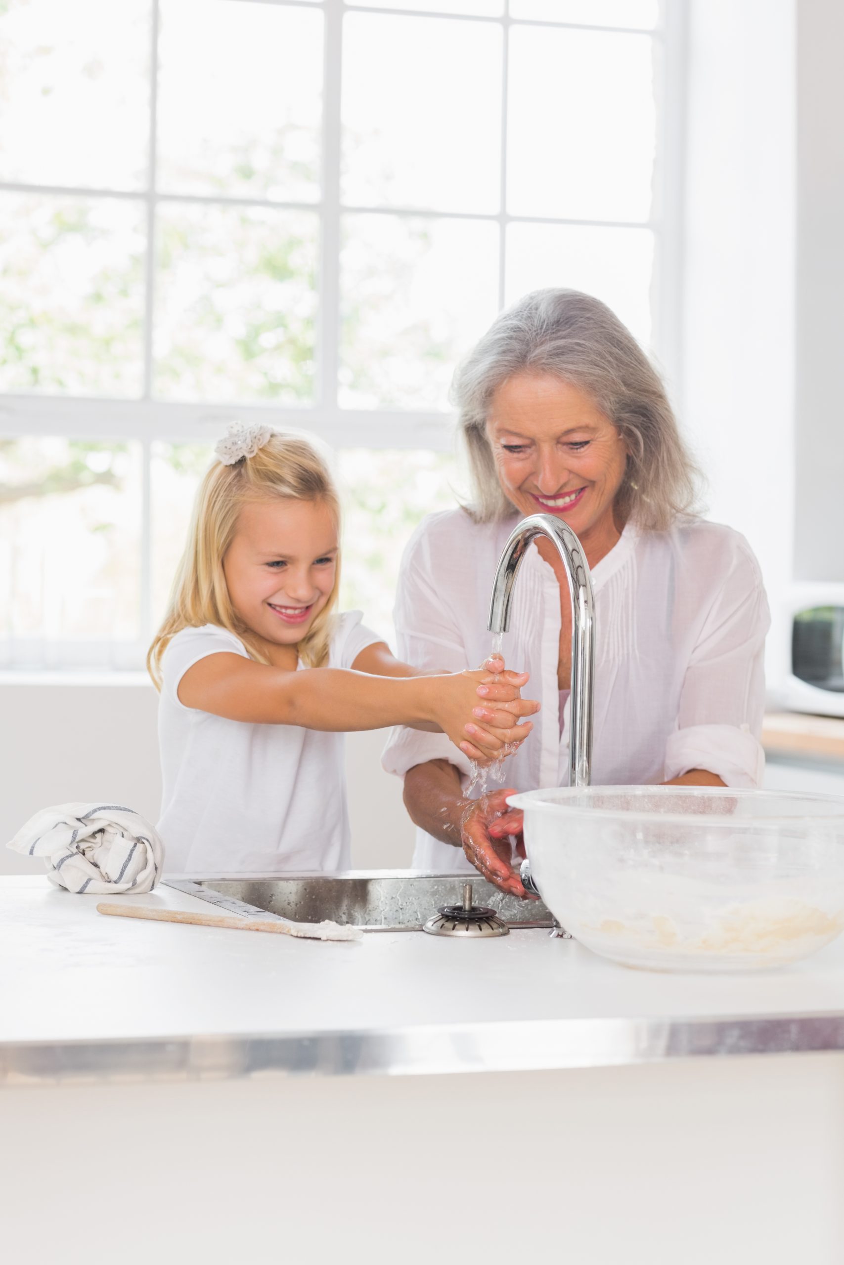 smiling woman and young girl washing hands in the kitchen