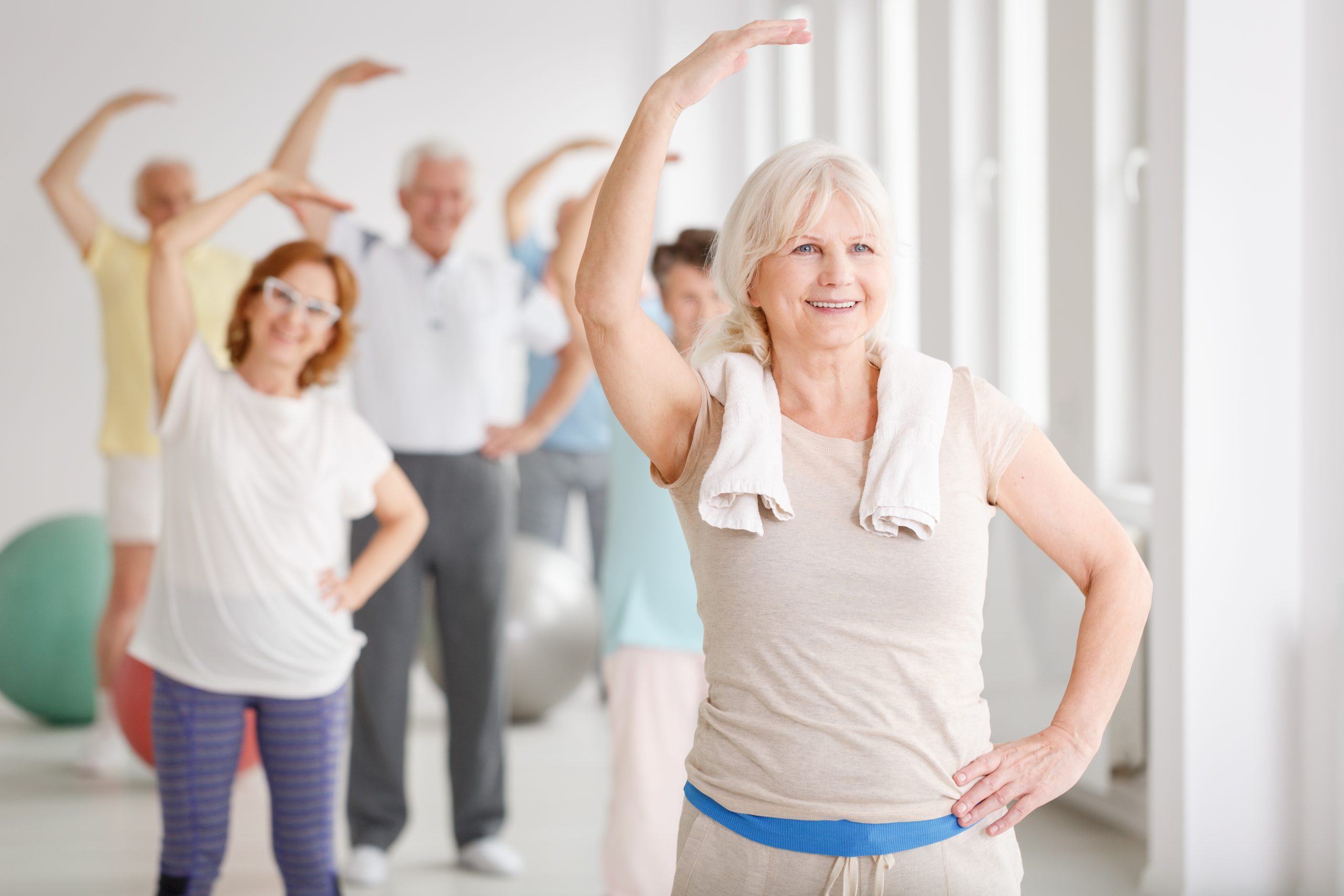 Older woman leading an exercise class of senior citizen adults arm stretches